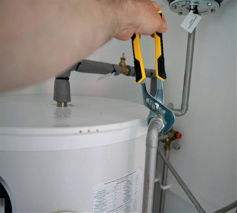 Hands tightening a fitting on top of a water heater