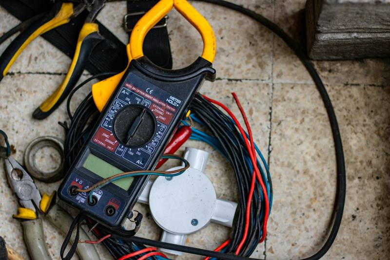 A clamp meter, pliers and cable laid out on a work floor